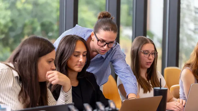 UNE students collaborate on a laptop around a conference table