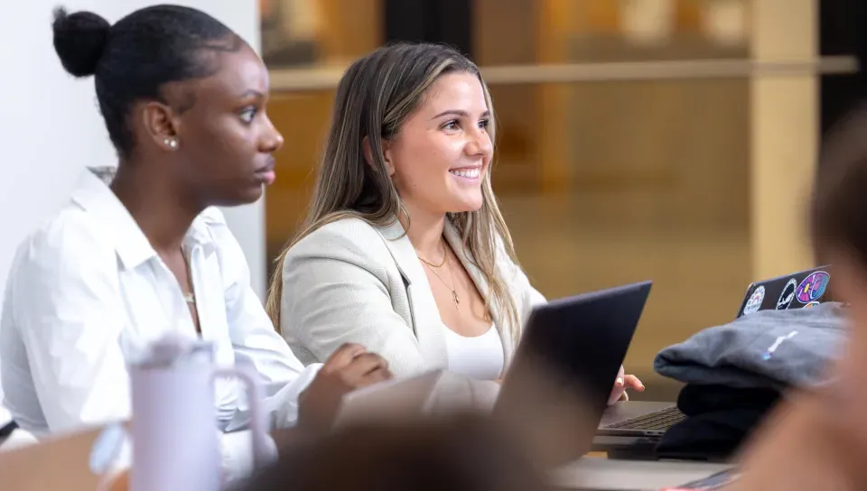 Two women business students work on their laptops